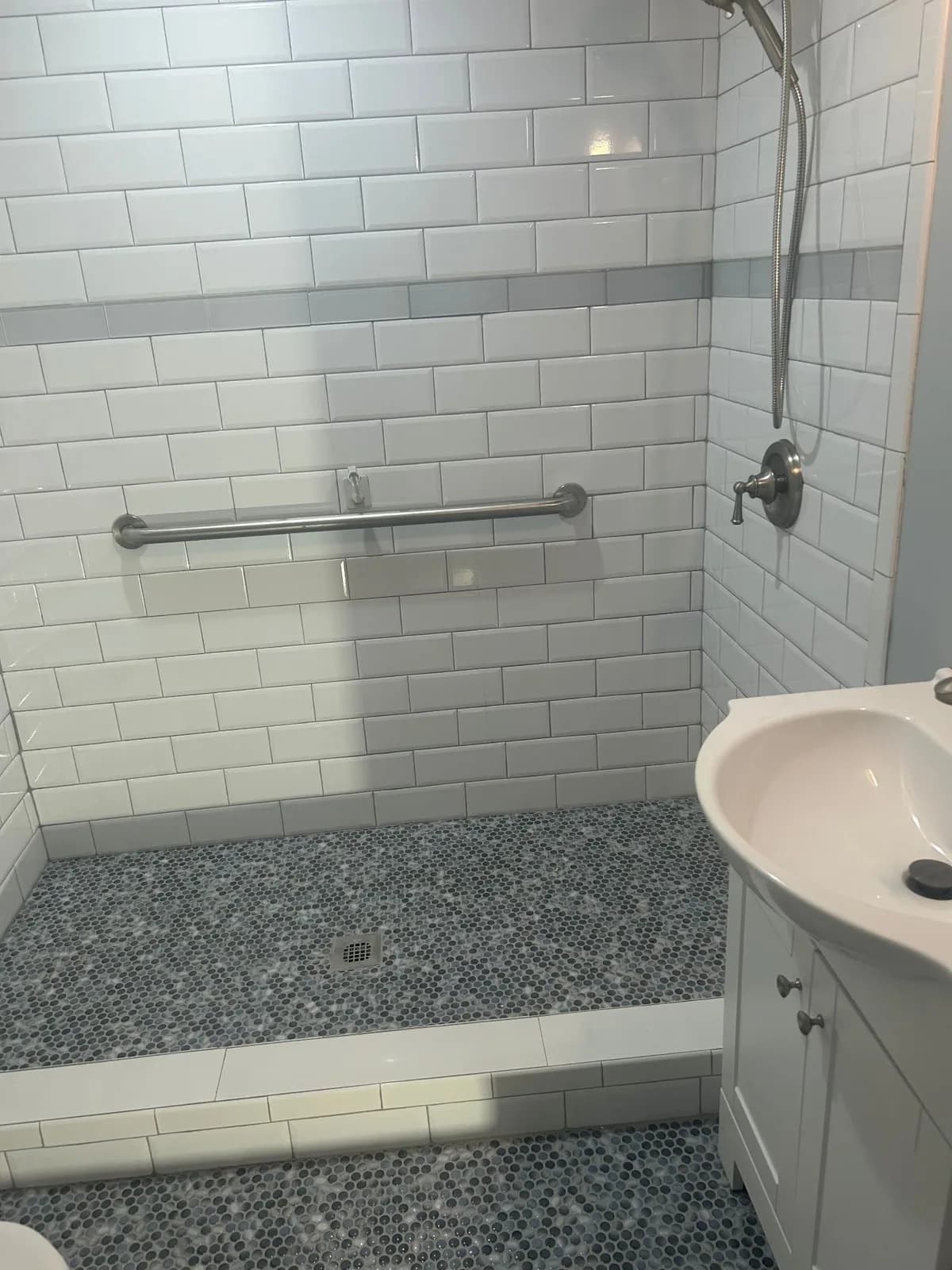 Tiled walk-in shower built by All Purpose Anytime Services with white subway tile, a penny-round mosaic floor and a grab bar