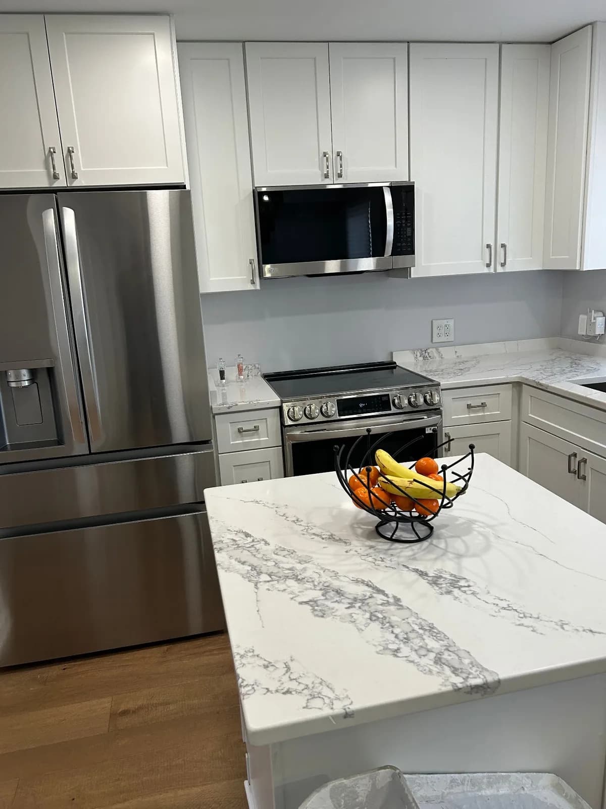 Kitchen remodel by All Purpose Anytime Services with white shaker cabinets, a quartz island and stainless appliances