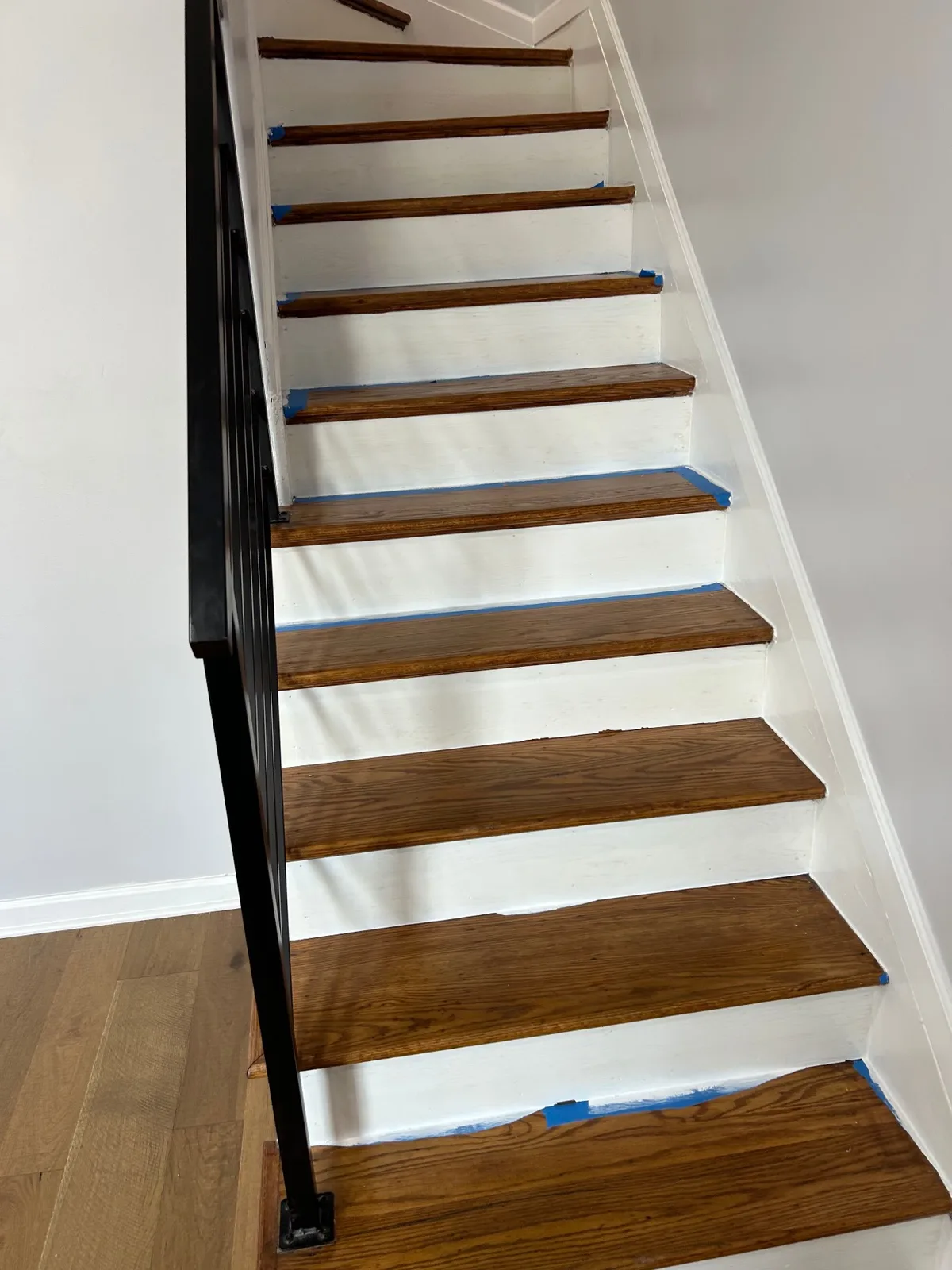 Refinished staircase by All Purpose Anytime Services with stained oak treads, freshly painted white risers and a black metal railing